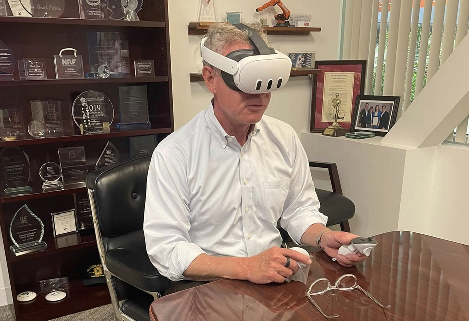 A member of Congress sitting at a table with a white Meta Quest 2 headset strapped to his head.