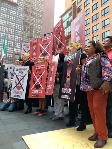 negotiations in Mexico City A group of people, some of them wearing Donald Trump masks, standing with protest banners